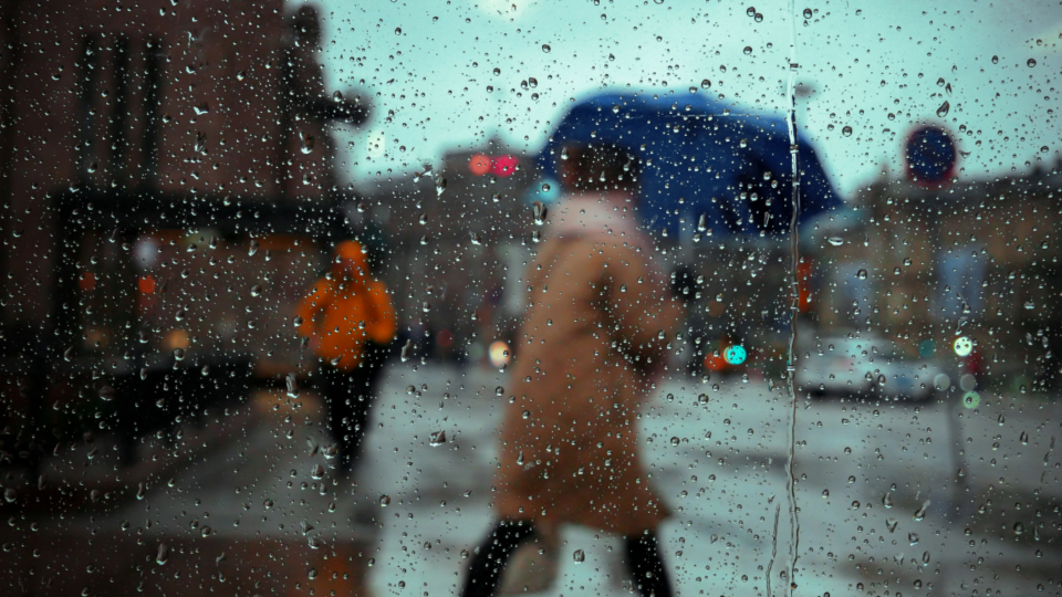 雨の街を歩く人を窓越しに見た風景